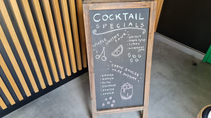 Blackboard with cocktail specials written on it. They include maple whiskey Sour and creme brulee white russian.
