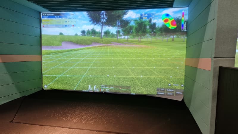 Image of the X-Golf system. There is a large screen with grass and trees.