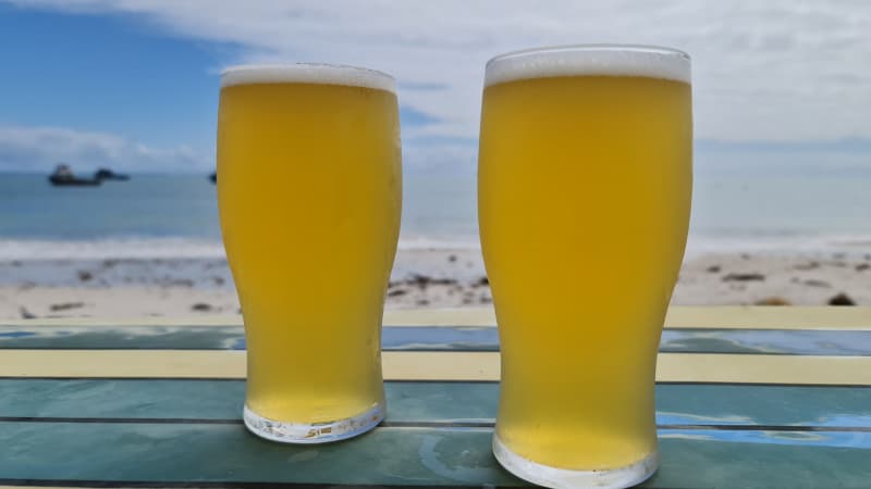 Two beers sitting on a surfboard table with the ocean in the background