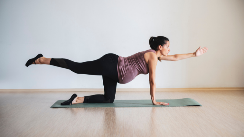 Pregnant woman in Pilates pose reaching one leg and arm out.