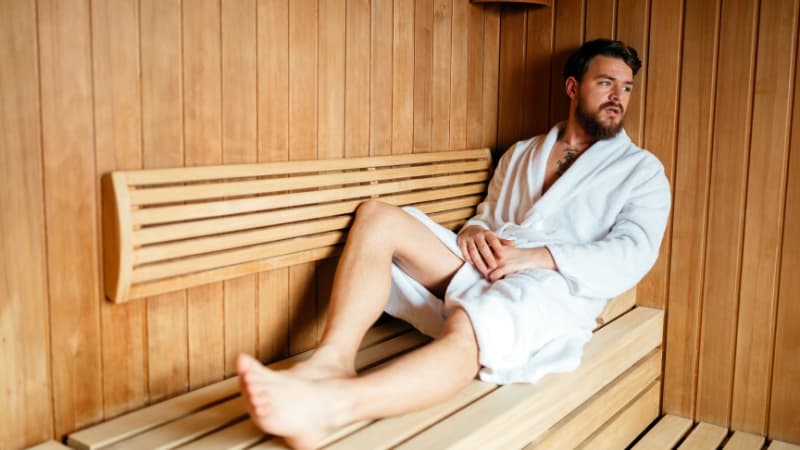 Man dressed in robe sitting in sauna