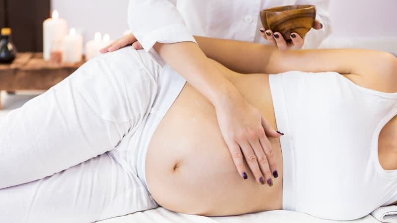 Person receiving Pregnancy massage. She is laying on her side and the therapist has her hand on her belly.