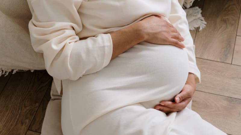 A woman wearing white, holding her pregnant belly