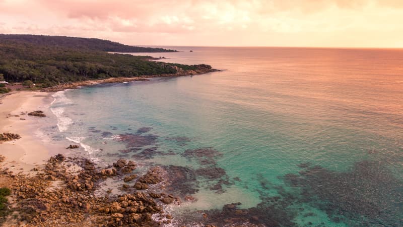 Castle Rock Bay at sunset. Sky is pink and ocean is a blue colour that fades to pink as it meets the horizon.