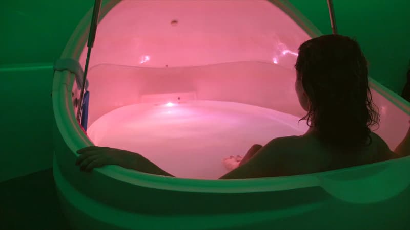 Woman sitting in a float pod that is glowing with pink light