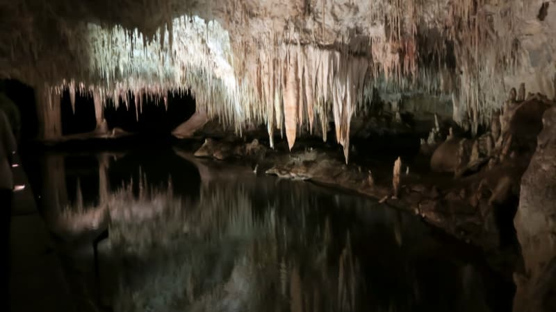 Underground lake in lake cave with white calcite stalactites hanging from the ceiling