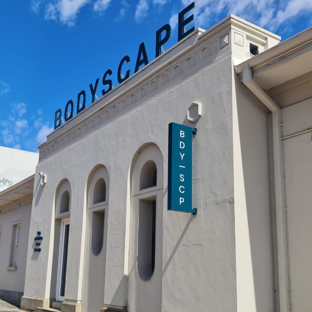 Exterior of Bodyscape Wellness Spa - white building with 3 arched windows and blue sign above that reads BODYSCAPE