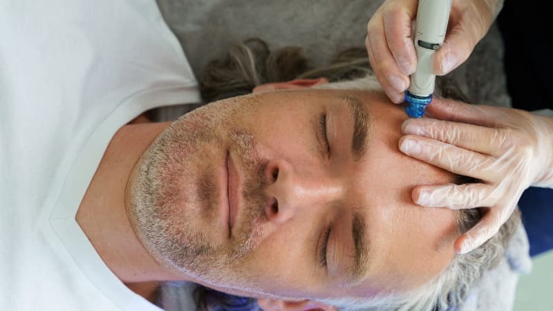 Man with grey hair and stubble receives a hydrafacial