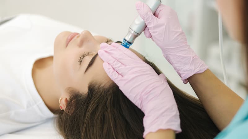 Therapist with pink gloves gives a woman with brown hair a hydrafacial
