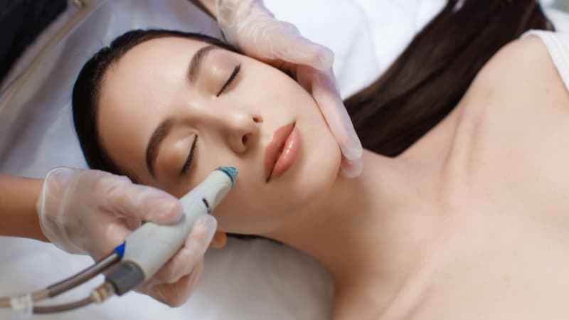 Woman with brown hair laying on her back as a dermal therapist gives her a hydrafacial
