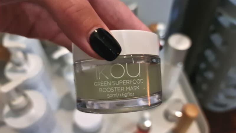 Hand with black nails holding iKOU Green Superfood Booster Mask