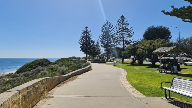 Cottesloe Foreshore path trails off into the distance. The ocean is to the left of the path, and grassy parklands to the right