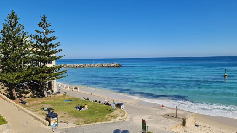 The rock groyne extending out into the bright blue water at Cottesloe Beach. The Indiana teahouse and pylon are also visible