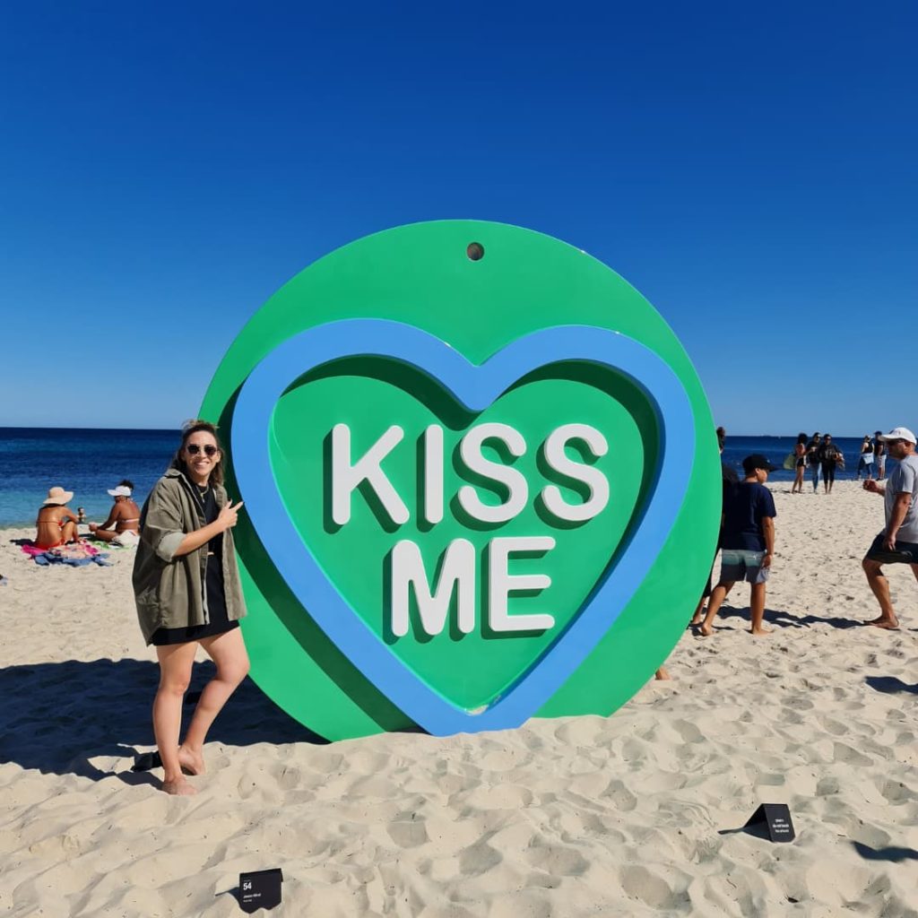 Huge green circular sculpture with a blue heart inside and the words"kiss me" in white