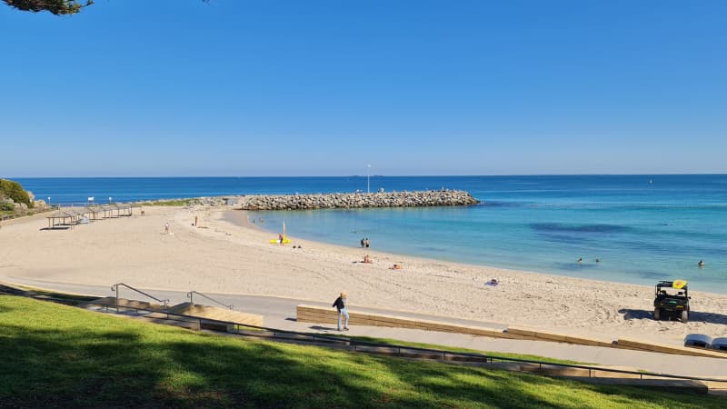 Rocks extend from the sand into the bright blue water at Cottesloe Beach