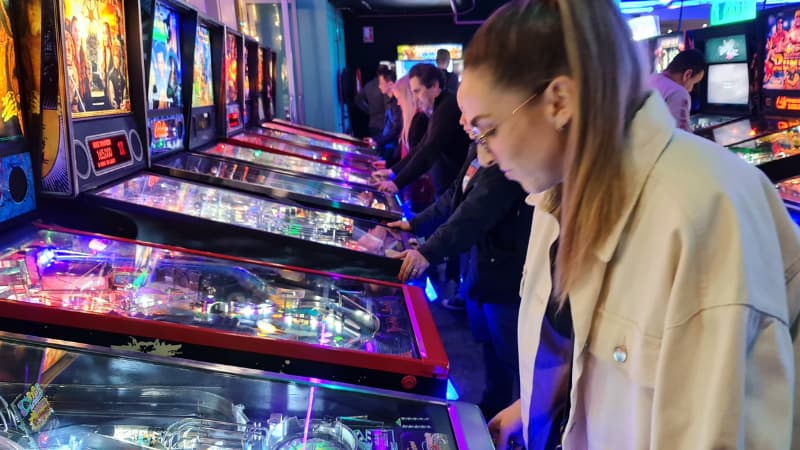 Row of pinball machines with people playing