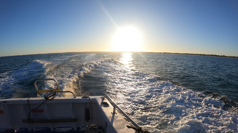 The sun rises over a boat heading out fishing offshore in Jurien Bay