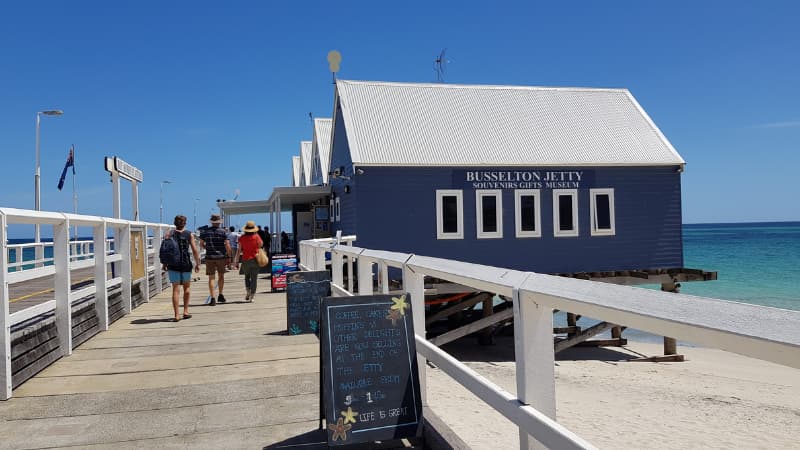 Blue buildings at the start of Busselton Jetty. There are people walking past 