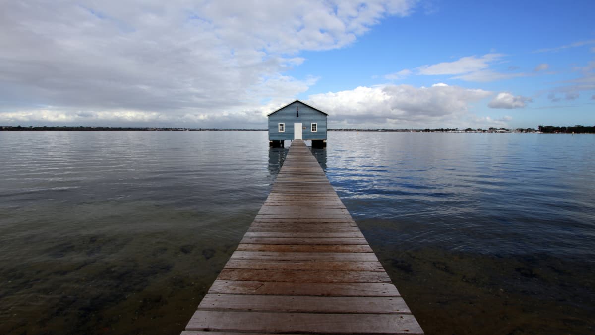 Perth's blue boatshed stands on clam water on a cloudy day