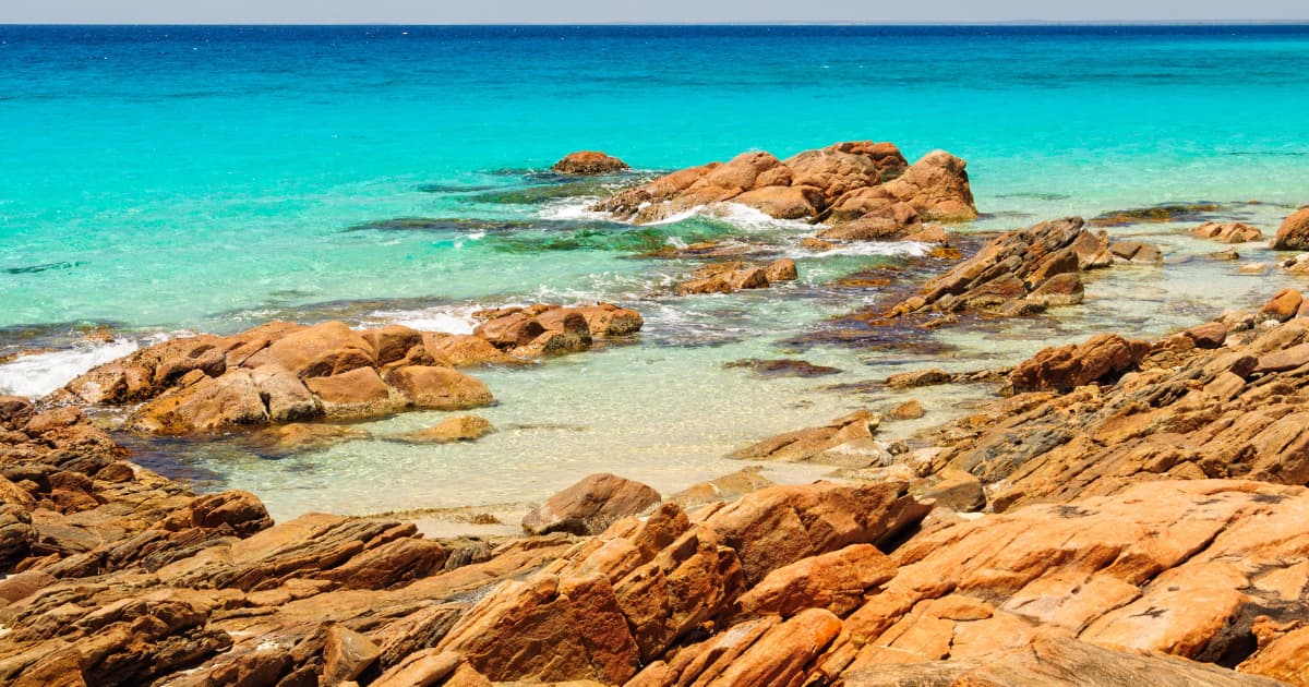 Rocky shoreline at Meelup Beach with turquoise water and clear blue sky.