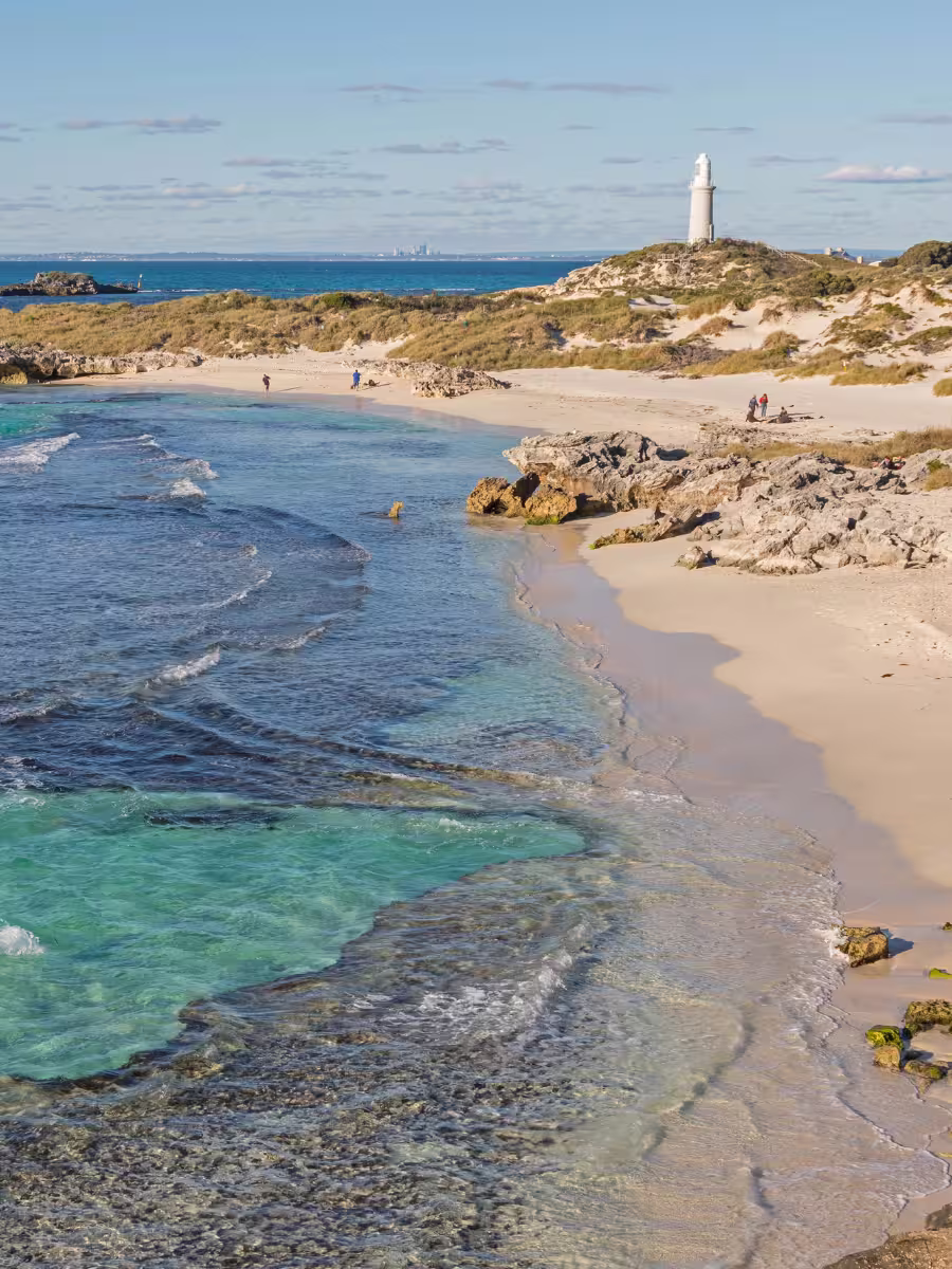 Rottnest Island Bathurst lighthouse Rottnest Island's coastline, featuring Bathurst Lighthouse standing on a grassy hill overlooking pristine turquoise waters and a sandy beach