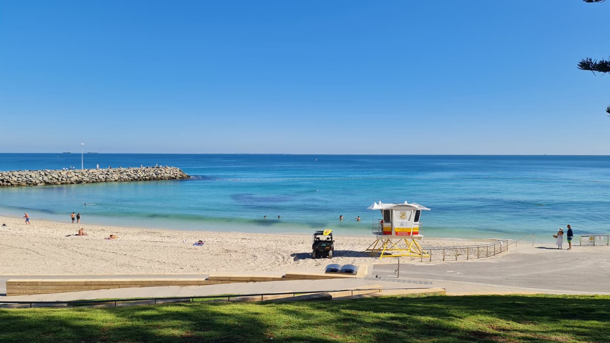 Cottesloe Beach People relaxing and swimming at Cottesloe Beach in Perth, with clear blue water, a rocky groyne, and a white lifeguard tower under a bright blue sky.