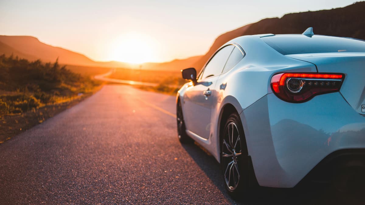 White sports car parked on an open highway at sunset during a road trip