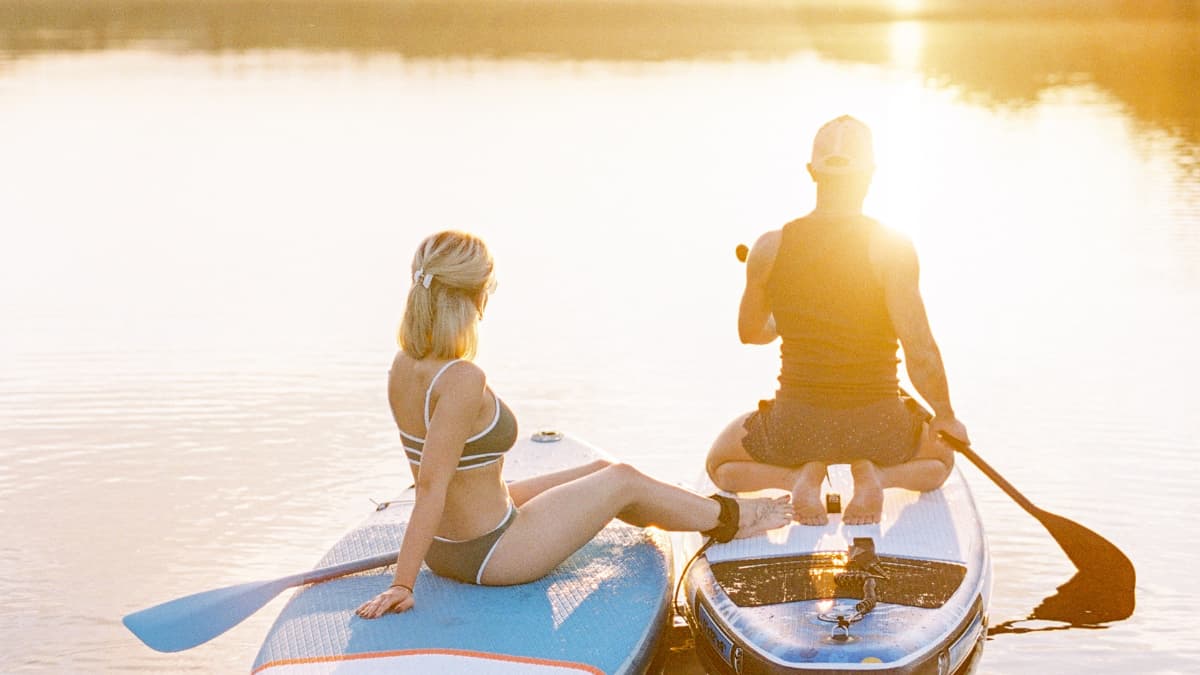 SUP.png from Squoosh Couple relaxing on paddleboards during golden hour on a still river