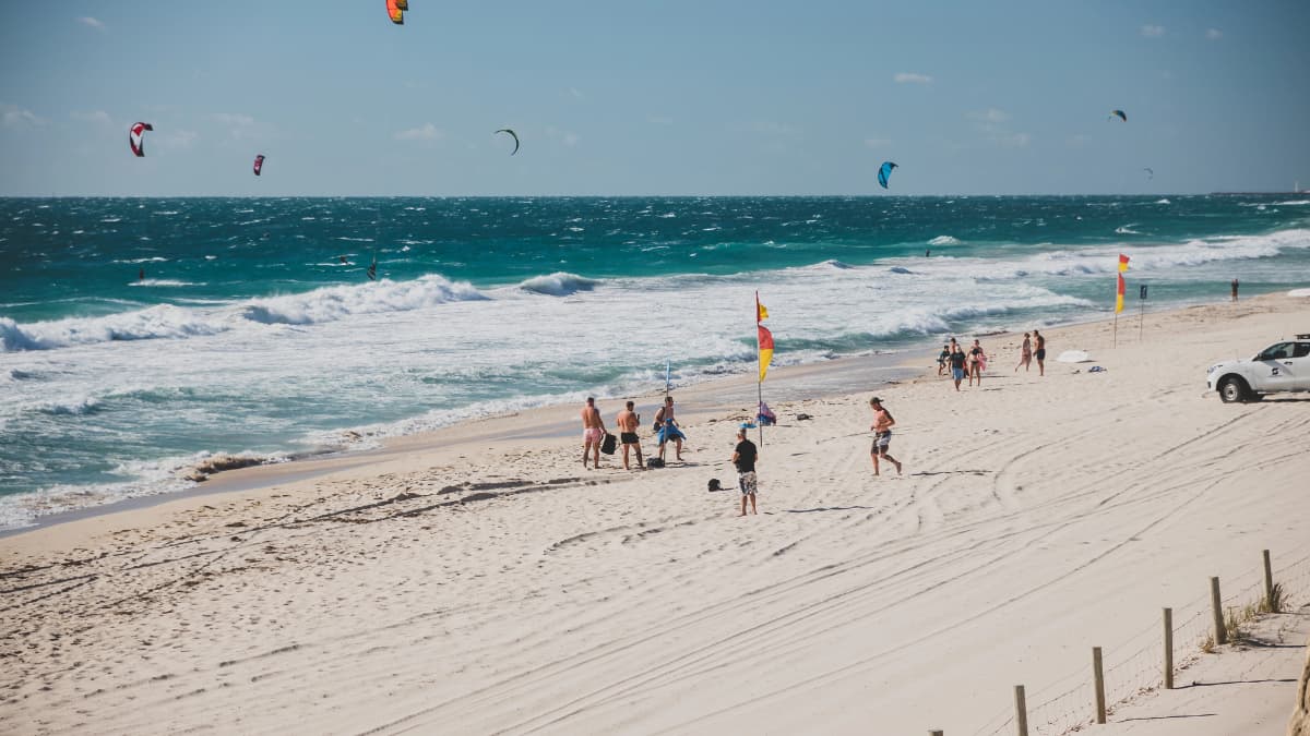 Scarborough Beach Windsurfer People kite surfing and swimming at Scarborough Beach with surf lifesaving flags and strong waves under clear blue skies