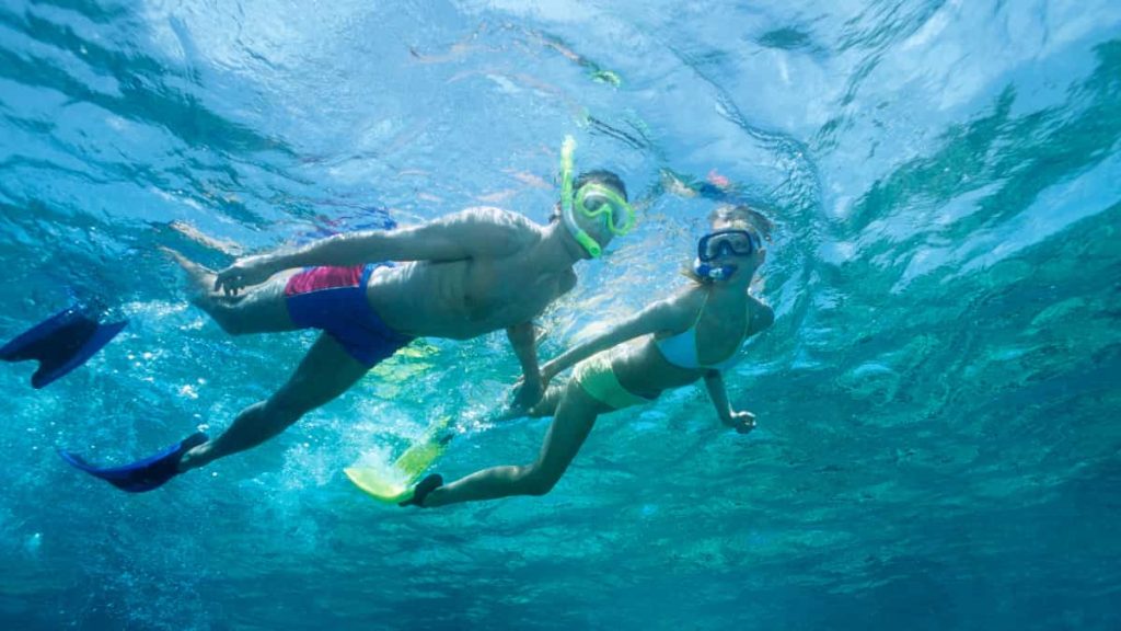 Couple snorkelling in clear turquoise water over coral reef