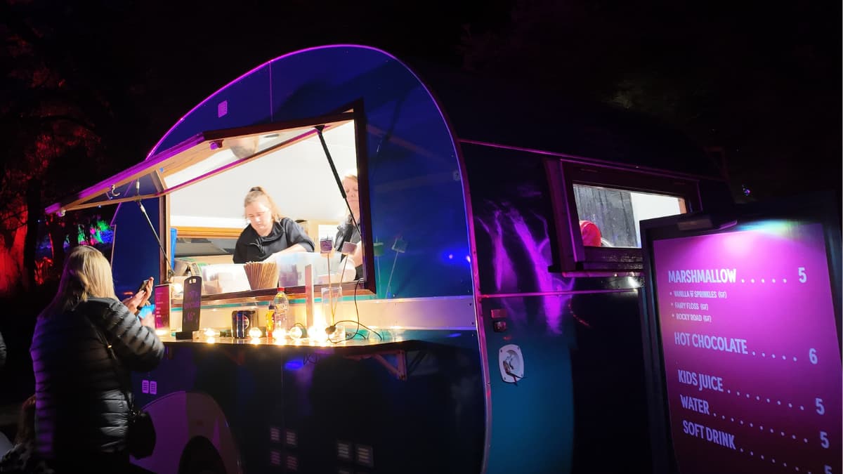 Lightscape Food Truck A curved, retro-style food truck bathed in purple light serving marshmallows and hot chocolates at Lightscape, Kings Park, Perth.