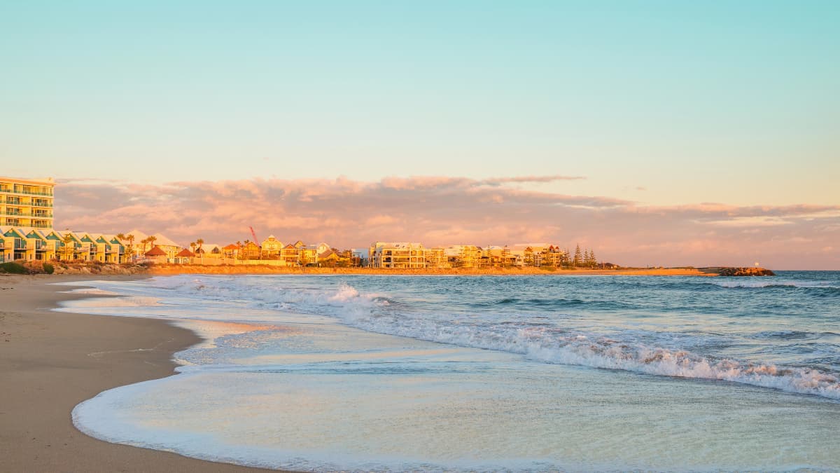 Golden sunset over Mandurah Beach with gentle waves, sandy shoreline and waterfront apartments in Western Australia.